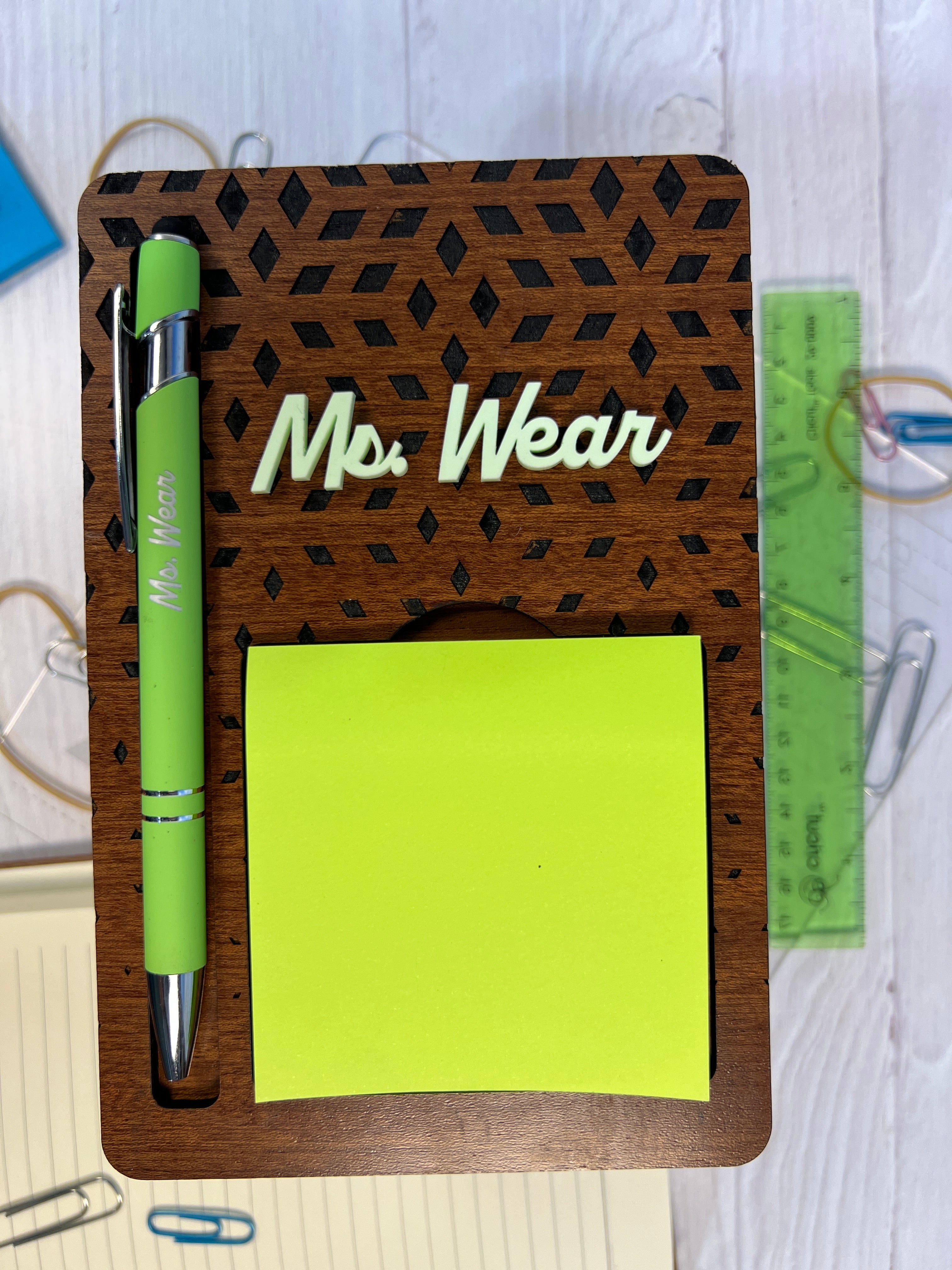 Wooden desk organizer with a green pen and sticky notes on a white surface.