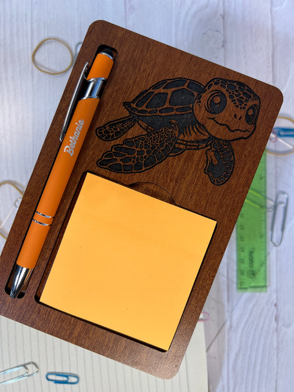 Wooden desk organizer with turtle design, pen, and sticky notes on a white surface.