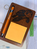 Wooden desk organizer with turtle design, pen, and sticky notes on a white surface.