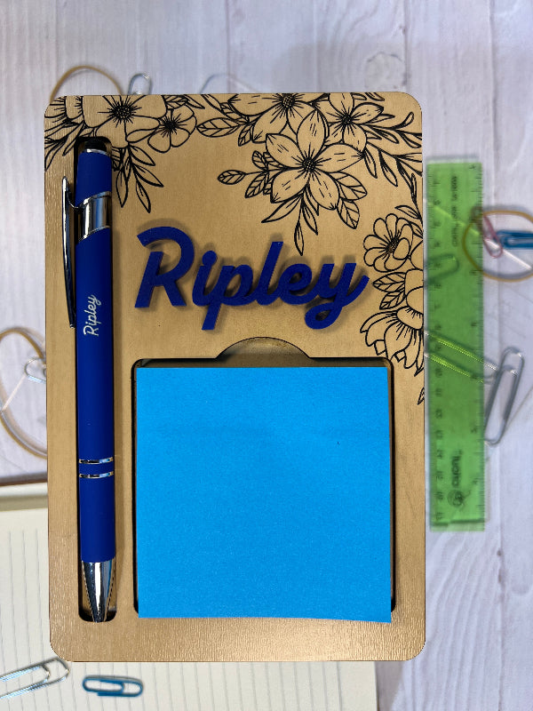 Notebook with floral design, blue sticky notes, and a pen on a white surface. From She Shed Designs