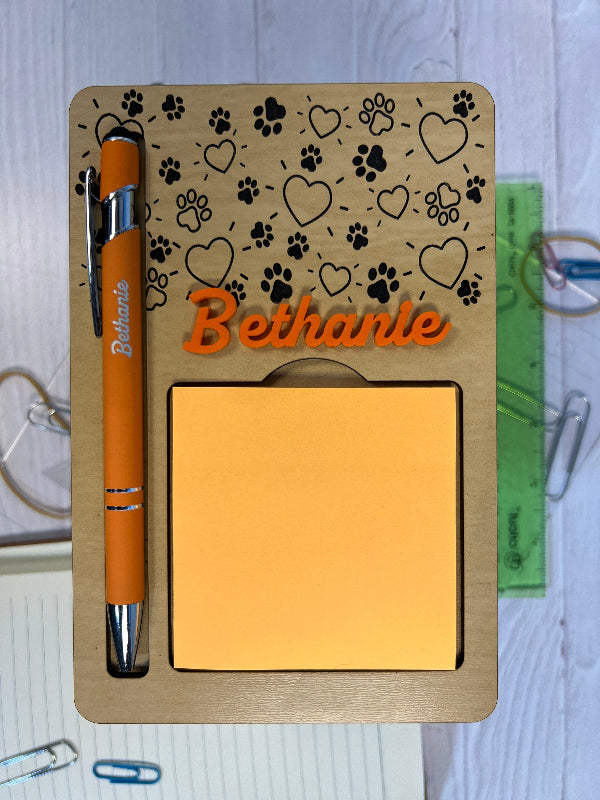 Holder with engraved pen and sticky notes on a textured surface. From She Shed Designs