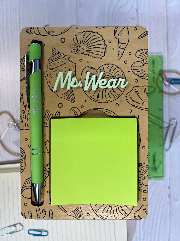 Holder with a green pen, and sticky notes on a white surface From She Shed Designs