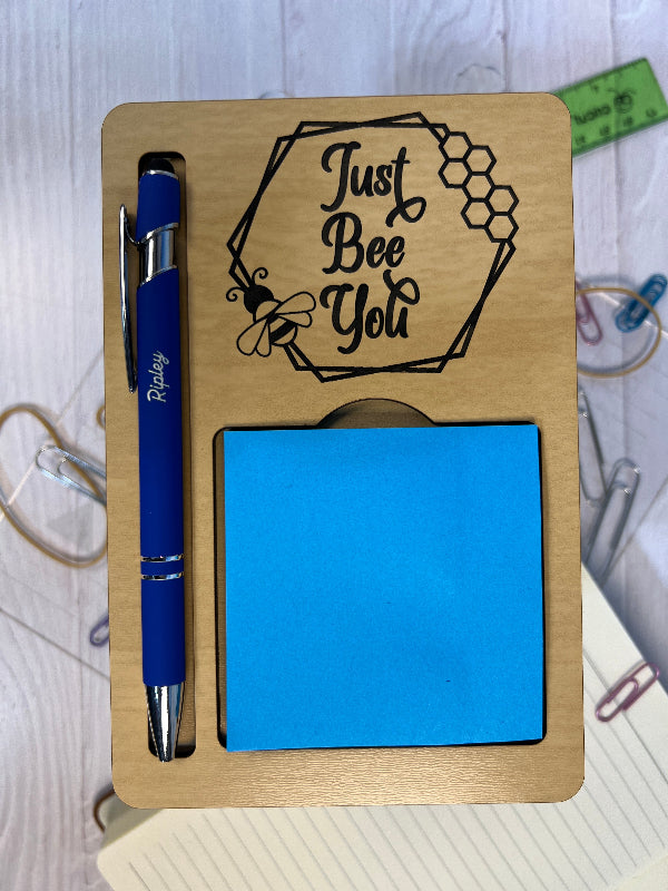 Wooden desk organizer with a pen, sticky notes, and decorative text on a light surface.