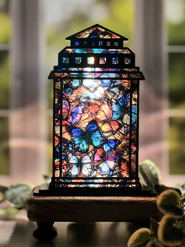 Faux Stained glass lamp with butterfly design on a wooden base, blurred greenery in the background. From She Shed Designs