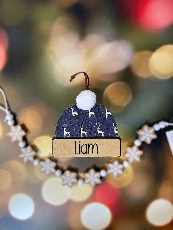 Decorative ornament with 'Liam' nameplate against a blurred Christmas tree background From She Shed Designs