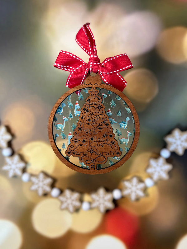 Wooden ornament with intricate dinosaur design on a Christmas tree. Layered behind with Dinosaurs wearing Santa hats. From She Shed Designs