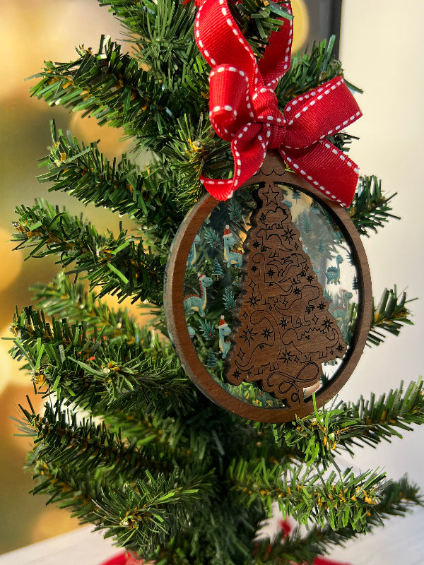 Wooden ornament with intricate dinosaur design on a Christmas tree. Layered behind with Dinosaurs wearing Santa hats. From She Shed Designs
