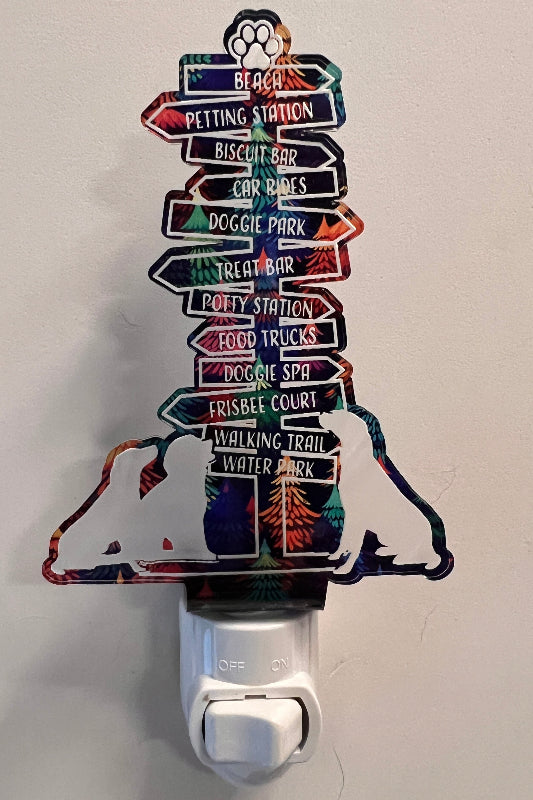 Handcrafted acrylic nightlight with a dog trail design, featuring multiple directional signs, plugged into a wall outlet. From She Shed Designs.