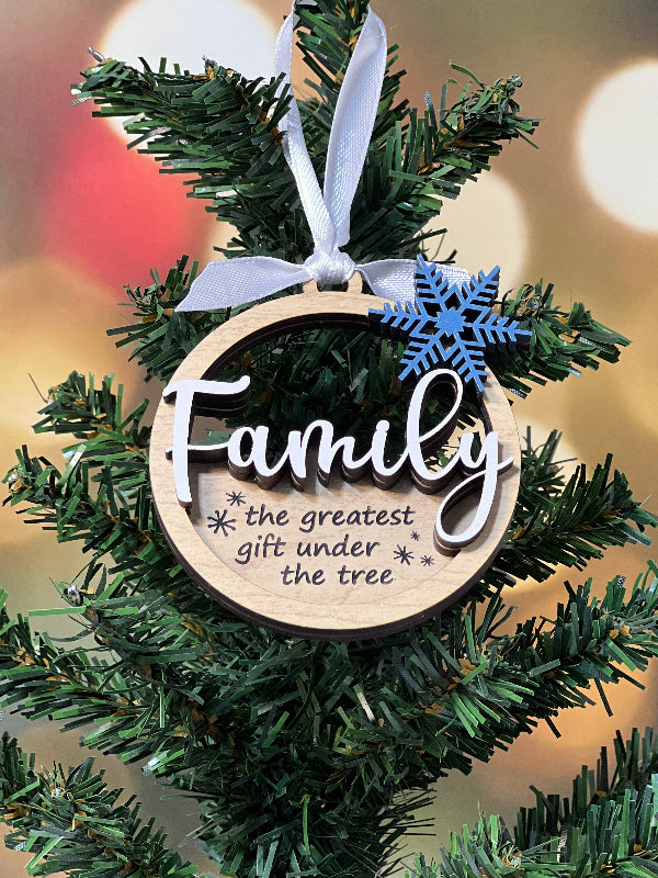 Decorative Christmas ornament with 'family the greatest gift under the tree' and snowflake design on a green branch. From She Shed Designs