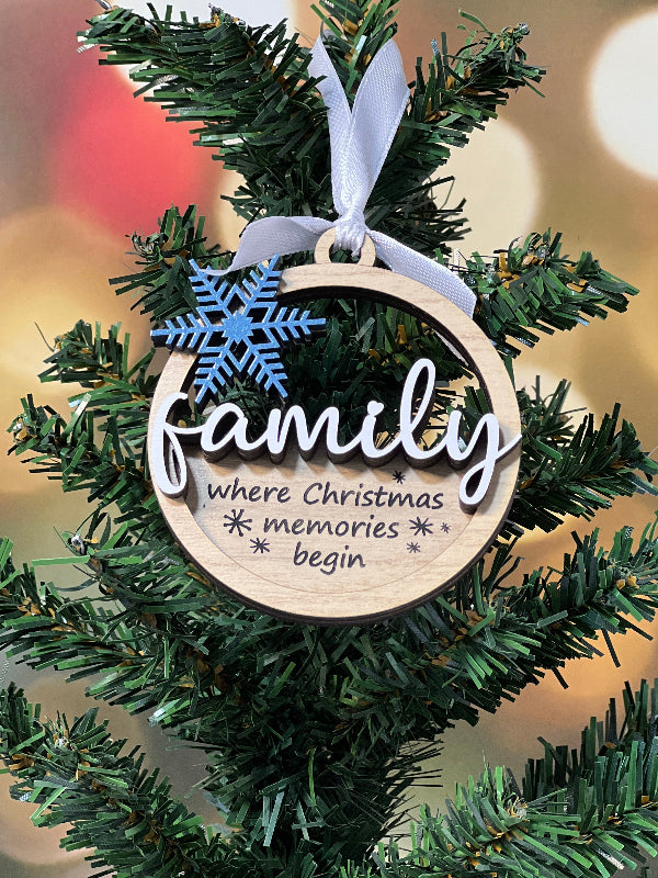 Christmas ornament with 'family where memories begin' text on a tree branch with blurred lights in the background. From She Shed Designs