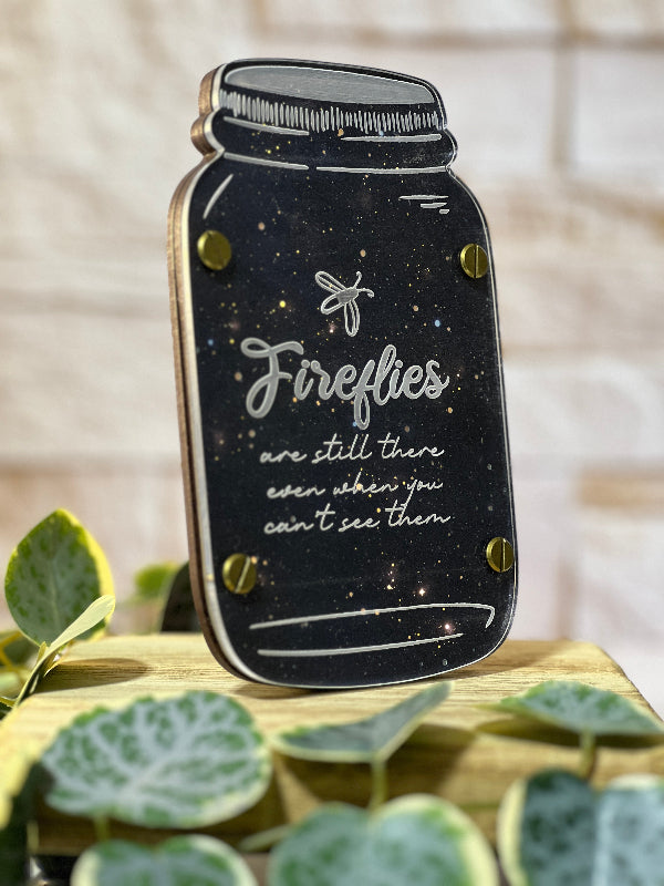 Mason jar-shaped night light with 'Fireflies are still there even when you can't see them' text on a wooden surface with leaves. From She Shed Designs