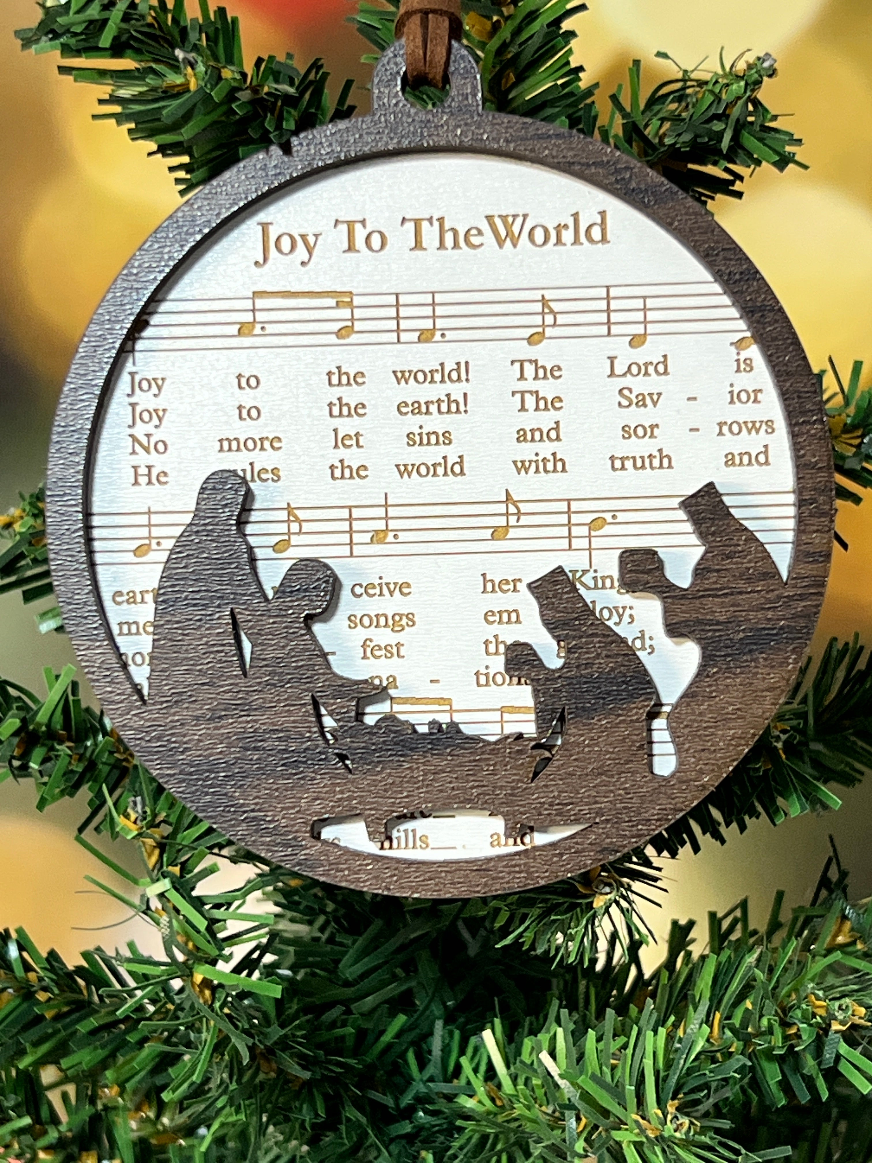 Decorative Christmas ornament with musical notes and manger scene silhouette on a green wreath. From She Shed Designs