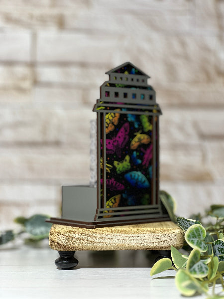 Decorative lantern with colorful insect design on a wooden base against a blurred background From She Shed Designs