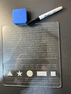 Transparent acrylic sheet with engraved letters, numbers and shapes, blue eraser, and dry erase marker on a dark surface. From She Shed Designs
