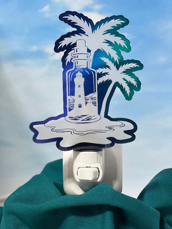 Decorative night light with lighthouse and palm tree design against a blue sky. From She Shed Designs.