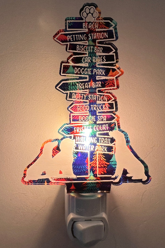Handcrafted acrylic nightlight with a dog trail design, featuring multiple directional signs, plugged into a wall outlet. From She Shed Designs.