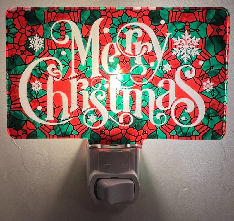 Handcrafted acrylic nightlight with a 'Merry Christmas' design, featuring a red and green patterned background with white cursive text, placed on a white surface. From She Shed Designs.