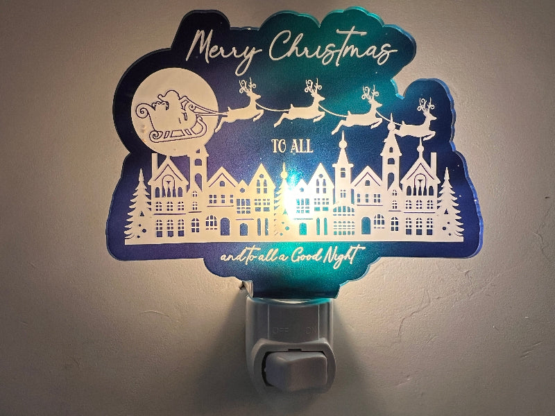 Handcrafted acrylic nightlight with a Christmas theme, featuring reindeer and houses, glowing in a dark setting. Says Merry Christmas to all and to all a good night. From She Shed Designs.