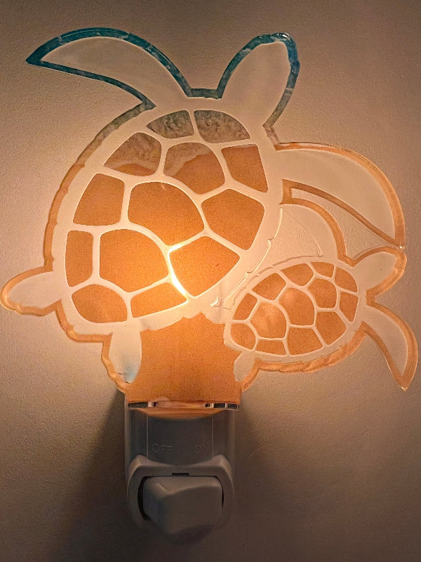Handcrafted acrylic turtle-shaped nightlight glowing in a room, showing a mother turtle with a baby turtle design. From She Shed Design.