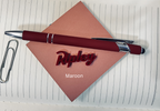 Maroon pen with silver clip on a pink paper with 'Ripley' branding, placed on lined paper. From She Shed Designs