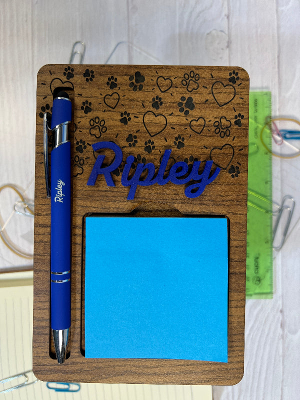 Wooden desk organizer with blue sticky notes, pen, and decorative elements on a white surface.