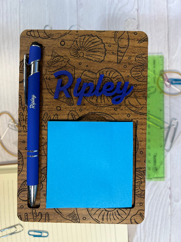 Wooden desk organizer with blue sticky notes, pen, and decorative elements on a white surface. From She Shed Designs