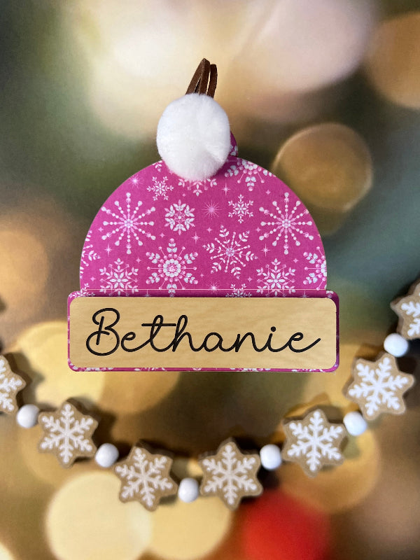 Decorative name tag with pink snowflake design and 'Bethanie' text on a blurred festive background. From She Shed Designs