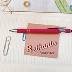 Red pen on a piece of paper with 'Bethanie' and 'Rose Haze' text, surrounded by stationery items. From She Shed Designs