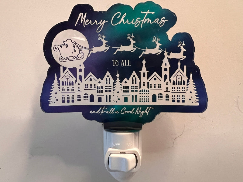 Handcrafted acrylic nightlight with a Christmas theme, featuring reindeer and houses, glowing in a dark setting. Says Merry Christmas to all and to all a good night. From She Shed Designs.
