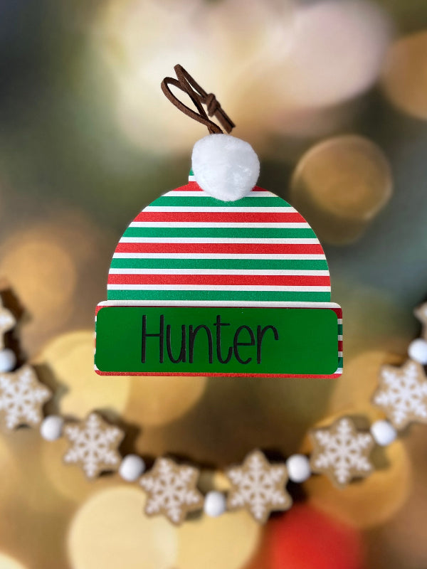 Decorative Ornament with a striped hat design and 'Hunter' text, against a blurred Christmas tree background. From She Shed Designs