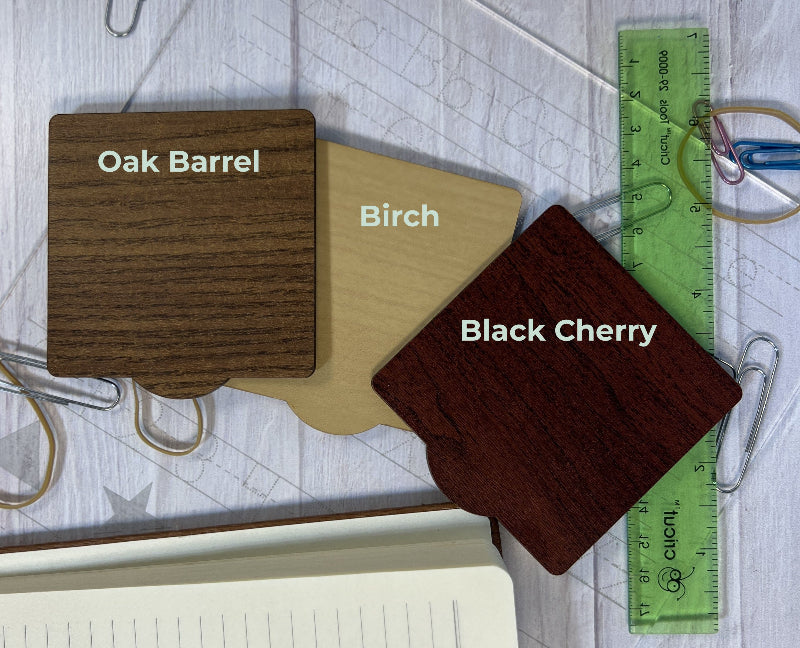 Three wooden samples labeled 'Oak Barrel', 'Birch', and 'Black Cherry' with a ruler for scale on a textured surface.