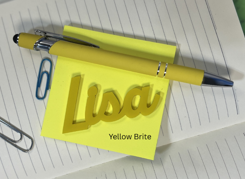 Yellow notepad with 'Lisa' on it, pen, and paper clips on lined paper. From She Shed Designs
